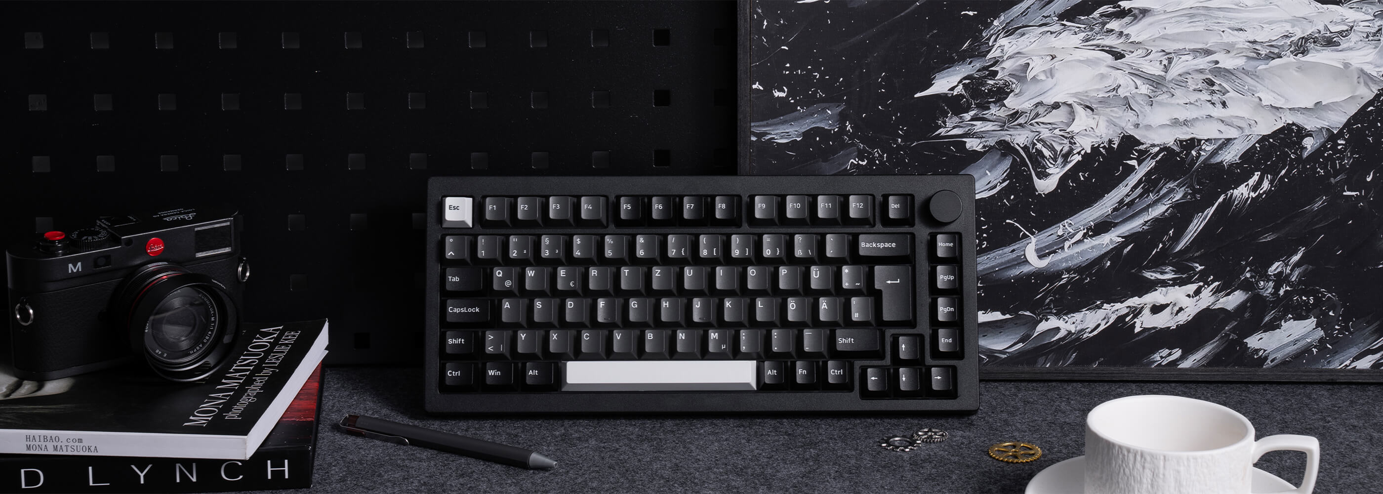 Auf dem Tisch liegt neben einer Kaffeetasse und einer Kamera eine Black & Silver 5075B Plus ISO-Tastatur